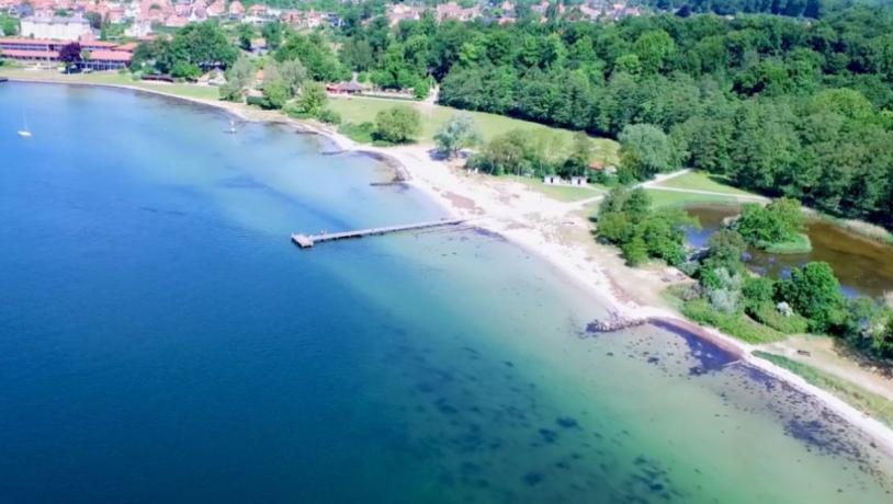 Strand set ovenfra med lyst sand og blåt og turkis vand.