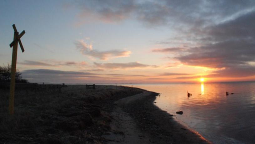 Smuk og rolig solnedgang på Hjortø. Den går ned over vandet, og i venstre side ligger marken hen i mørket.