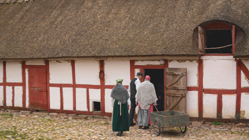 Et par mennesker iklædt tøj fra tidligere århundreder er på vej ind i et rød og hvidt bindingsværkhus