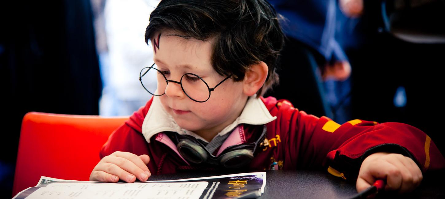 Dreng udklædt som Harry Potter til sidder og kigger på et stykke papir der ligger på bordet foran ham.