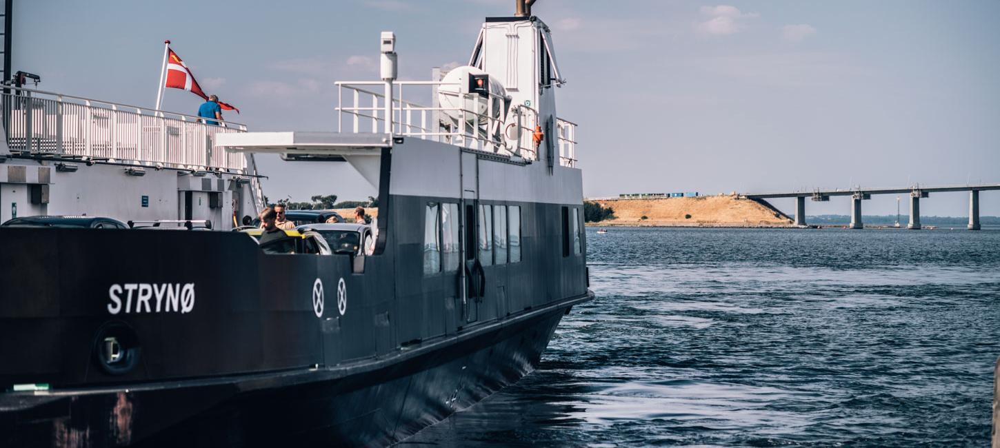  The Strynø ferry on the water with people on board, with a bridge visible ahead.