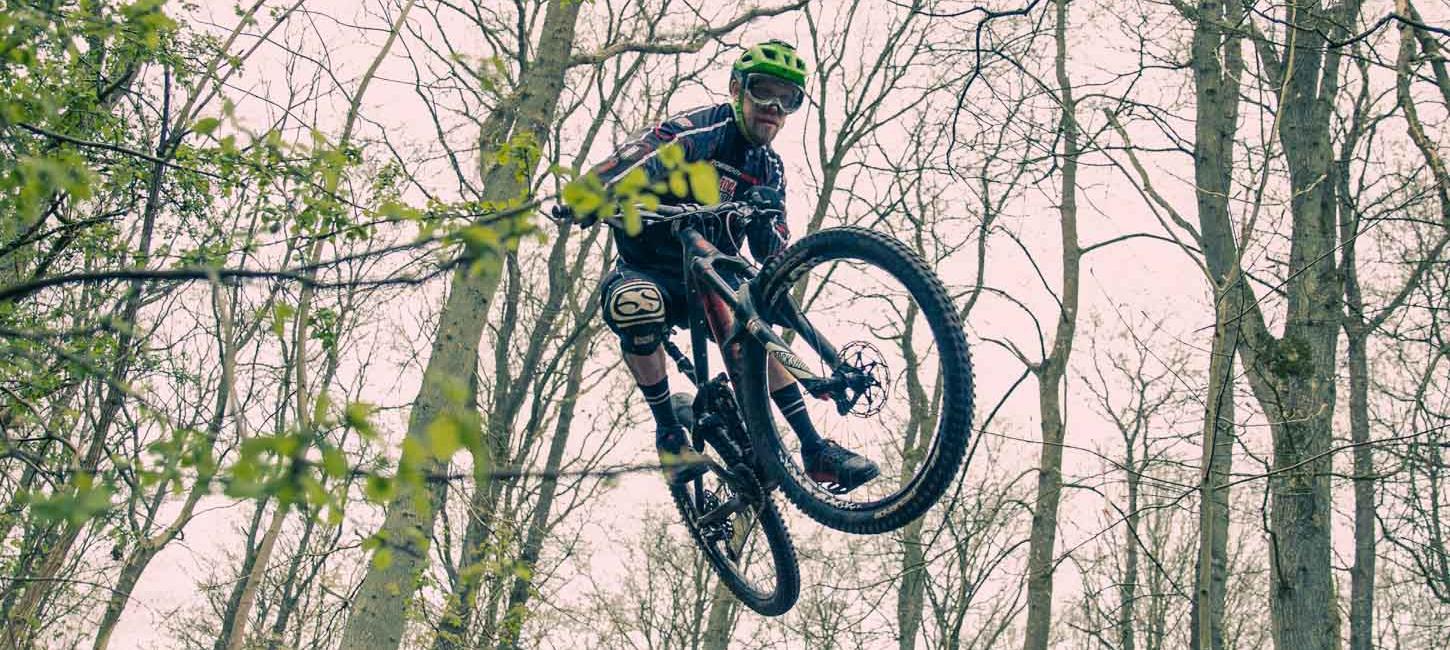 En mountainbiker med grøn hjelm, der er oppe i luften. 