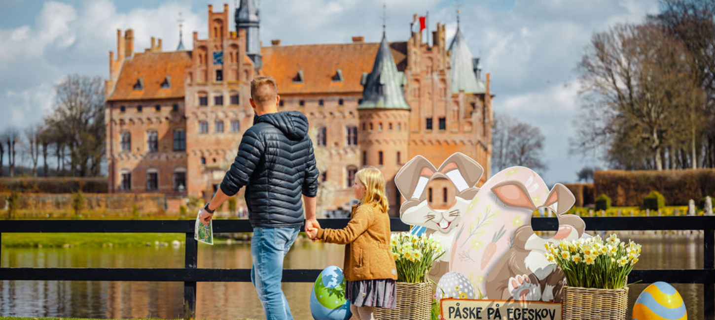 En far og datter går hånd i hånd med Egeskov Slot i baggrunden, og med påskedekoration omkring sig.