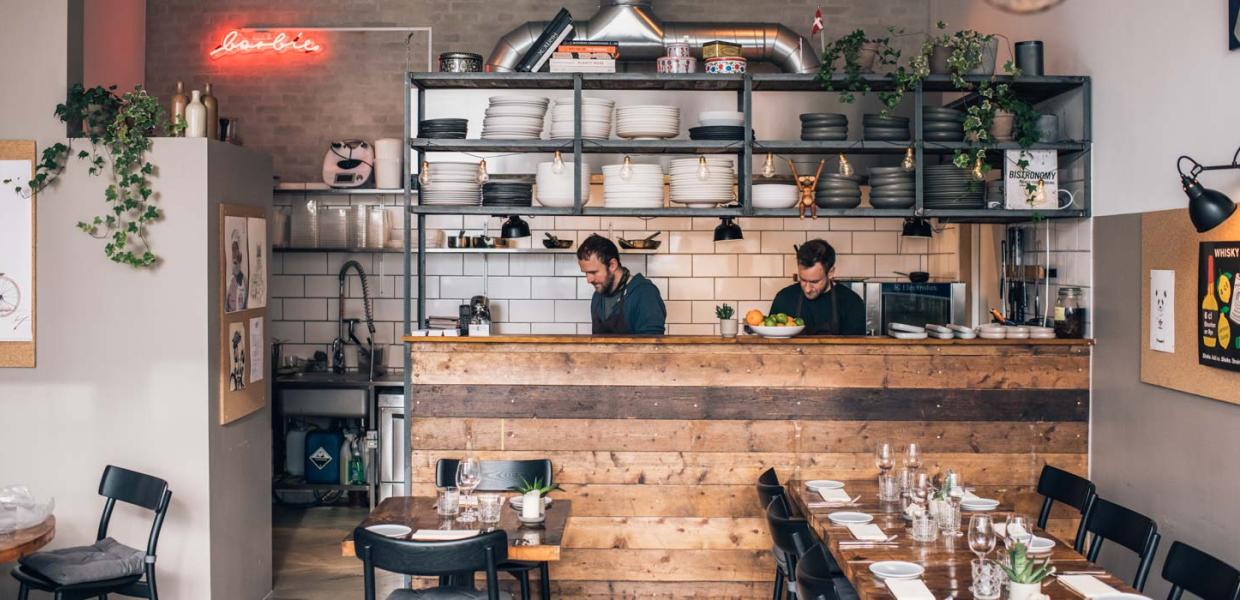 Et kig ind i et køkken på en restaurant, hvor to mænd står bag en høj disk af træ.