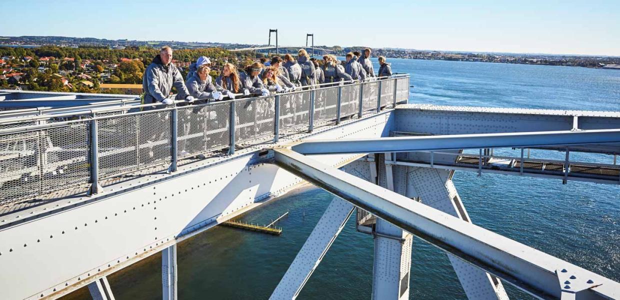 En flok mennesker på bridgewalking på den gamle Lillebæltsbro. Den nye Lillebæltsbro anes i baggrunden.