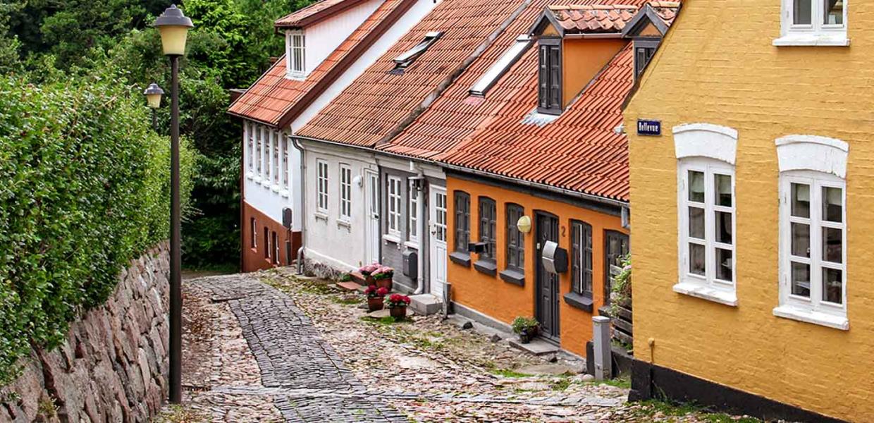 Gamle byhuse i orange og hvide farver på skrånende brostensbelagt gade i Assens