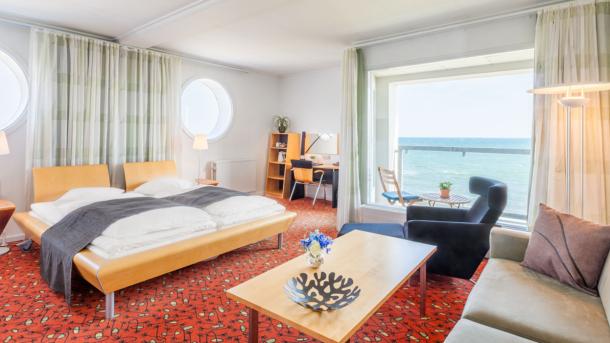 Hotelværelse med stor dobbeltseng og afslapningshjørne, med udsigt over havet.