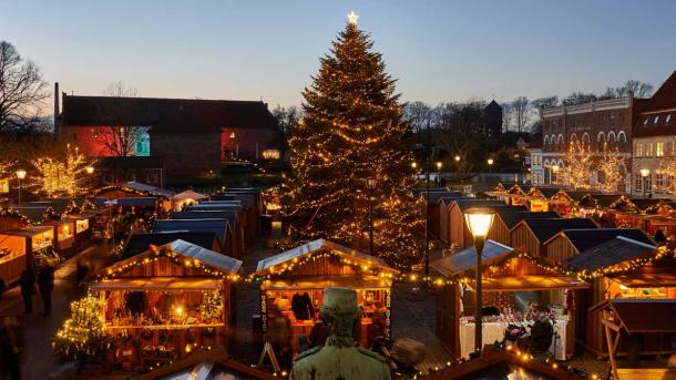 Hyggeligt julemarked set lidt oppefra med varme lys og et stort juletræ i midten.