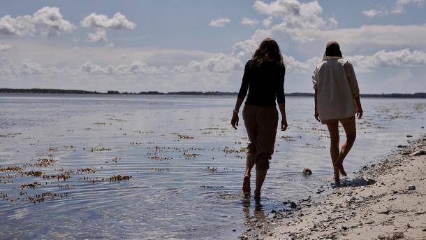 To kvinder går i vandkanten iført sommertøj 