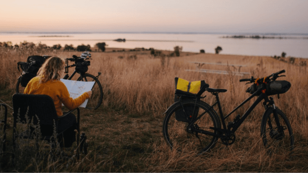 Kvinde sidder i en campingstol ved siden af ​​sit telt og cykler og ser på et kort i den gyldne time og forbereder sig til næste dags cykeltur