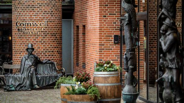 Indgangsparti ved hotel af røde mursten med gamle tønder og en statue af H. C. Andersen foran