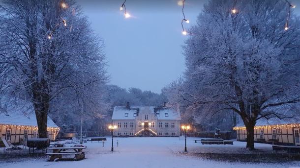 Et gammelt hus klædt i sne og med julebelysning