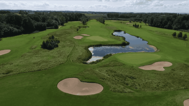 En golfbane med en sø, friskt grønt græs og omkranset af træer