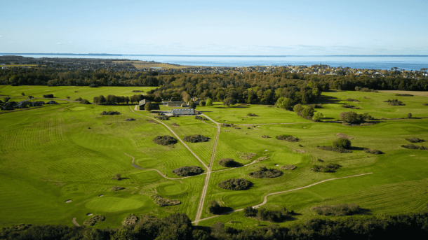 Dronefoto af grøn golfbane med træer og stier