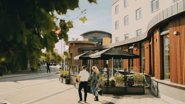 En træbelagt facade ud til et torv, hvor der går en mand og kvinde