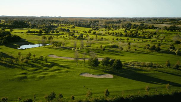 Grøn golfbane med grupper af træer, bunkers og en lille sø