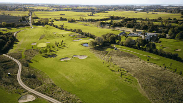 Luftfoto af golfbane med træer, stier og bunkers. 