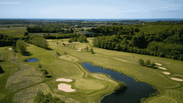 Grøn golfbane se fra luften med sandbanker, sø og omkransende træer 