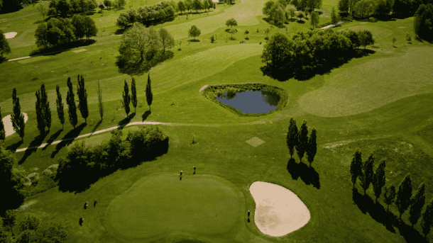 Dronebilleder af en grøngræsset golfbane med sandbanker, søer, træer og golfspillere