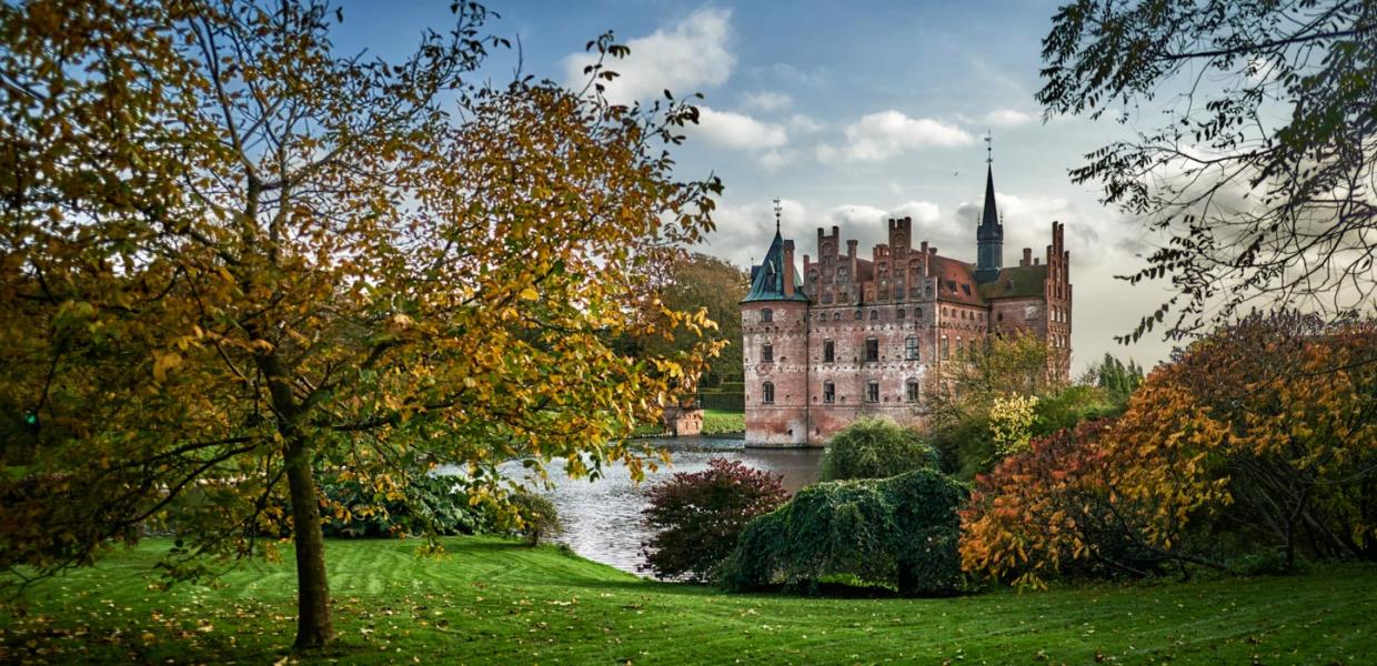 Egeskov Slot omgivet af træer og buske i efterårets farver.