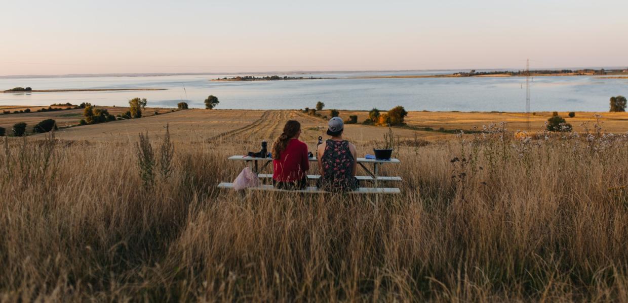 To kvinder sidder med ryggen til og kigger ud over en masse marker med vand i baggrunden.