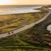 To cyklister cykler på smal grussti lige ud til vandet ved en fynsk strand. I baggrunden ses en smuk solnedgang. 