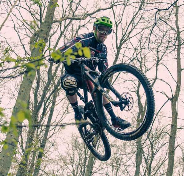 En mountainbiker med grøn hjelm, der er oppe i luften. 