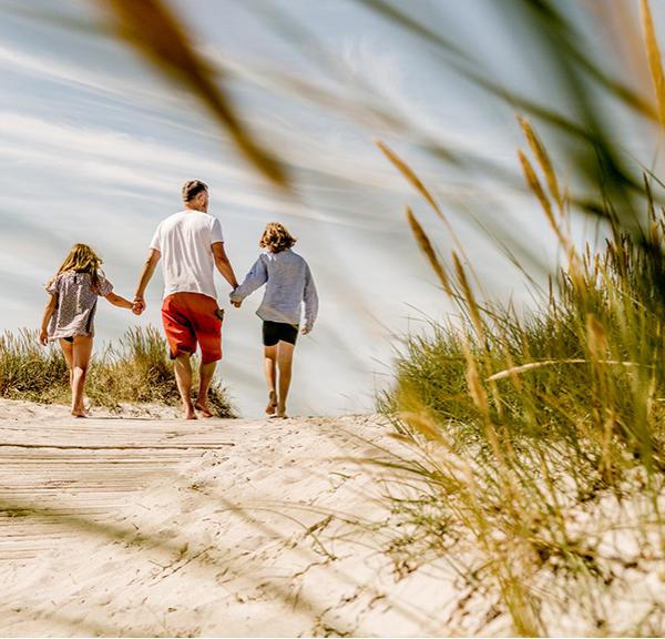 En familie går hånd i hånd på en strand.