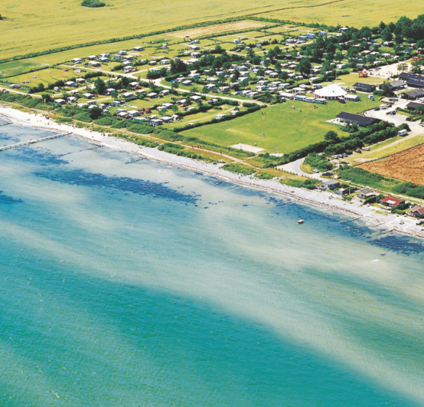 Luftfoto af Camp Hverringe, som ligger omkranset af marker lige ud til en hvid og lavvandet strand