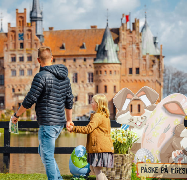 En far og datter går hånd i hånd med Egeskov Slot i baggrunden, og med påskedekoration omkring sig.