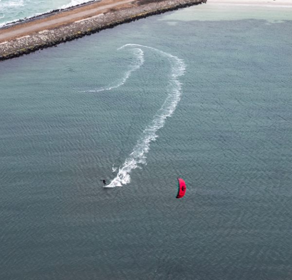 En kitesurfer med rødt sejl driver på stille vand ud for en dæmning