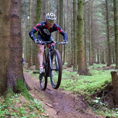 En mountainbiker i skoven, omringet af træer og vildt mos.