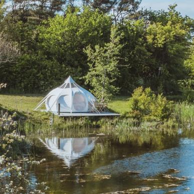 Hvidt glampingtelt i naturskønne omgivelser ned til vandet.