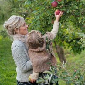 Kvinde og barn plukker rødt æble fra æbletræ.