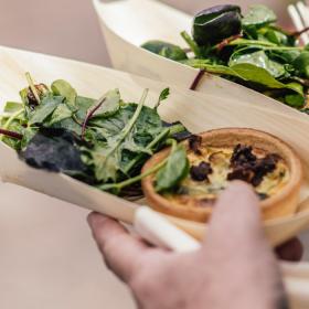 Hånd holder snack-bakker med quiche og salat.