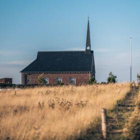 Landevej omringet af marker i varme farver og med en kirke i baggrunden.