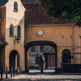 Kvinde på vej ind gennem port i gammel bygning i Assens. Uret over porten viser, at klokken er 17.45.