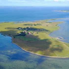 Dronebillede af Hjortø. Øen er både omgivet af blåt vand og himmel. 