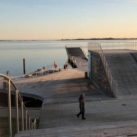 En stor badebro med udspringsmuligheder og havet i baggrunden, der genspejler en blå og gullig himmel