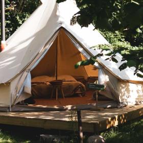 Glampingtelt med lille terasse foran står i grønne naturomgivelser.