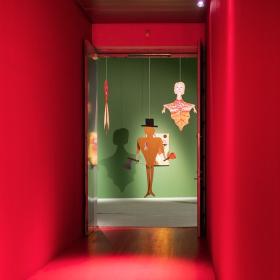 Rødt rum. Gennem et hul i den røde væg ses nogle udstillede genstande, der hænger ned fra loftet foran en grøn væg.