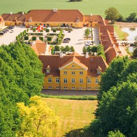 Et dronebillede af Broløkke Herregård med grønne marker og skov