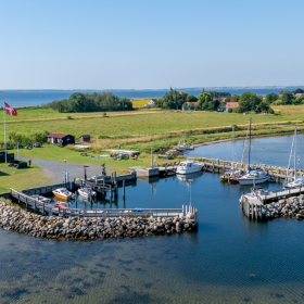 Dronebillede af Hjortø. Øen er både omgivet af blåt vand og himmel. 