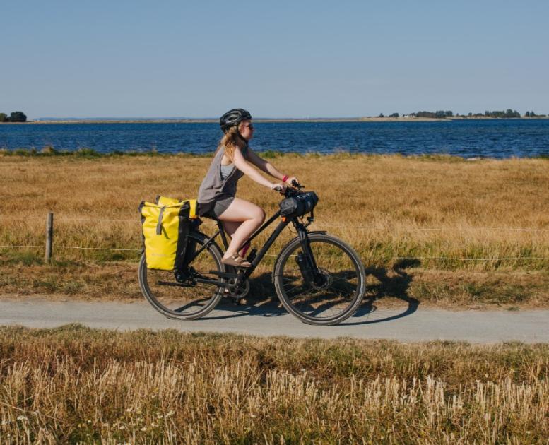 Kvindelig cyklist med oppakning og cykelhjelm på sti ud til havet om sommeren.