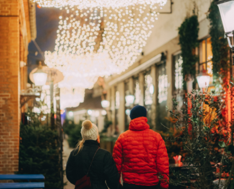 Et par holder hænder på vej ned ad en gade med lyskæder hængende ovenover dem